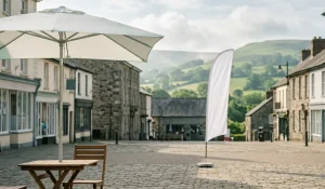 A peaceful AI generated, sunlit market square in Newtown, Powys, featuring a blank white custom-printed parasol and feather flag against a backdrop of rolling green hills.