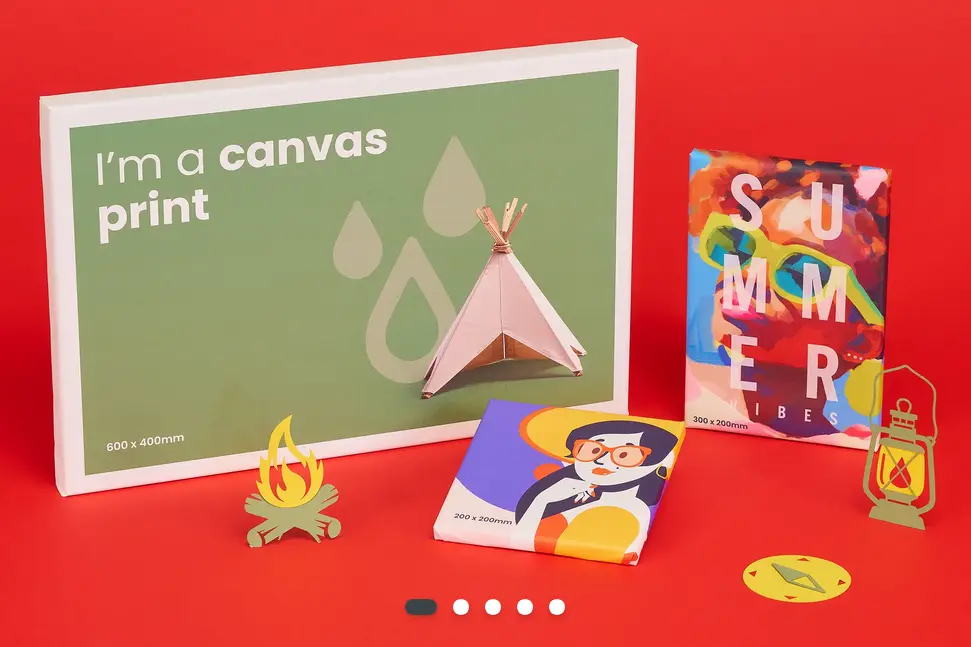 Three canvas prints are displayed together. One is 600x400mm, one is 200x200mm, one is 300x200mm. The largest canvas print has the words I'm a canvas print printed on it. They are set against a vibrant red background with printed cut-outs of campsite designs, which suits the happy summer theme of the canvas prints.