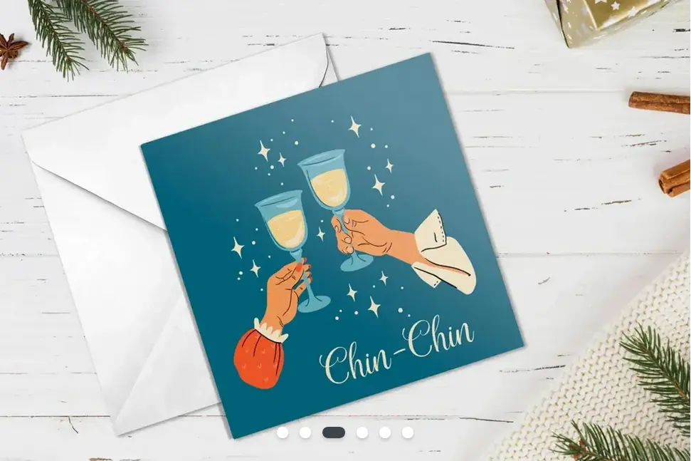 A Christmas card with a cartoon champagne glass design, with the words 'Chin-Chin'. The card is on a painted wooden table with sprigs of holly.