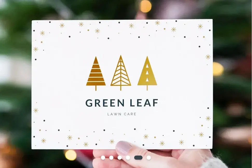 A hand holding up a business Christmas card for a lawn care company. The card has three gold Christmas tree icons in the centre and snowflakes around the edge.