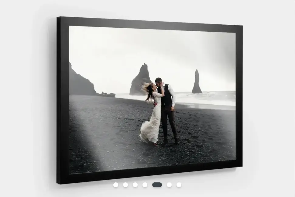 A photo print of a bride and groom on a beach in a black picture frame. Hanging on a wall.