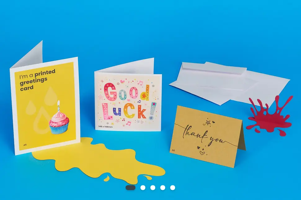 Three greetings cards set against a blue background with a stack of white envelopes. One of the cards says ' I'm a printed greetings card'.