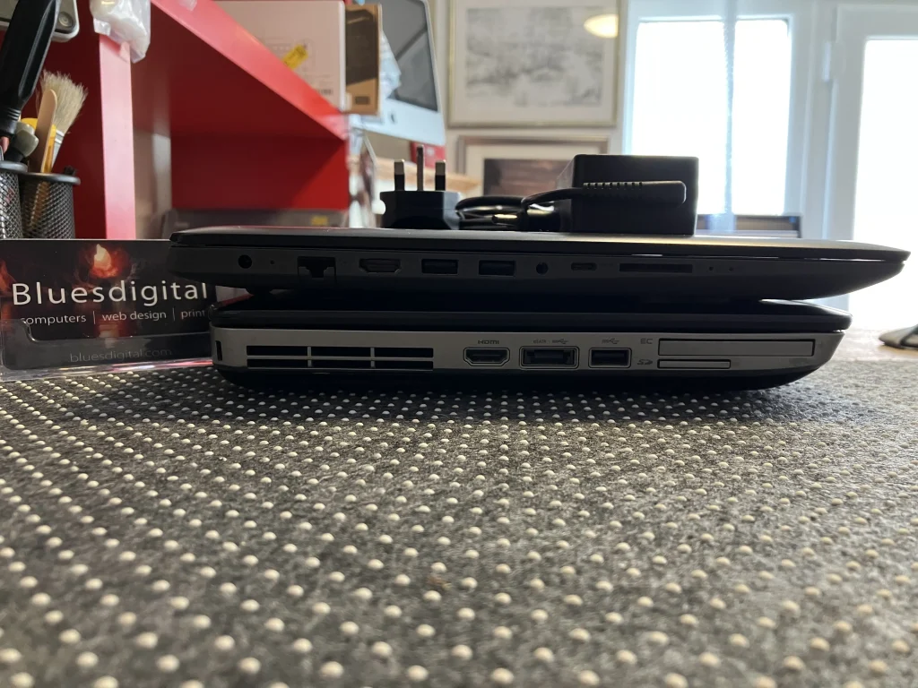 Image of a refurbished Lenovo laptop on top of an old Dell laptop showing the different ports and the difference in thickness. 