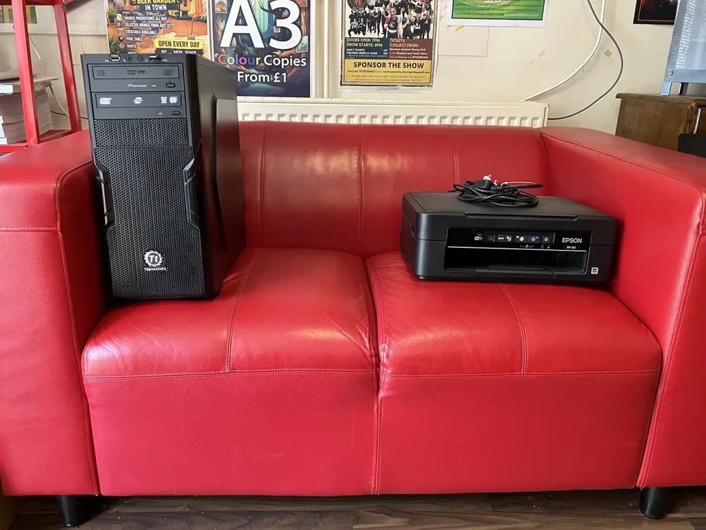 A photo of a PC and a printer sitting at opposite ends of the red couch in the Bluesdigital workshop in Newtown.